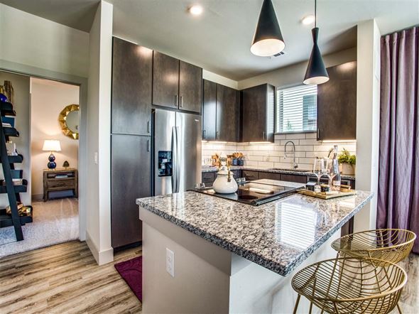 Grand Prairie apartment for rent - Two-Bedroom Apartments in Grand Prairie, TX - Waters Edge at Mansfield - Kitchen With Granite Island, Dark Wood Cabinets, Pendant Lights, Stainless Steel Refrigerator, And Bar Seating.