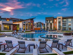 Grand Prairie apartment for rent - Pet-Friendly Apartments in Grand Prairie, TX - Waters Edge at Mansfield - Swimming Pool With In-Pool Lounge Chairs, Surrounding Sun Deck Seating, And Modern Apartment Buildings.