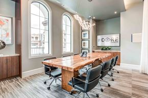 Chandler apartment for rent - Chandler, AZ, Apartments - The Core Chandler - Business Center Conference Room with Wood-Style Flooring, Large Wooden Table with Black Office Chairs, Various Built-In Shelving and Cabinetry, Large Windows, and Overhead Hanging Lighting Fixture.