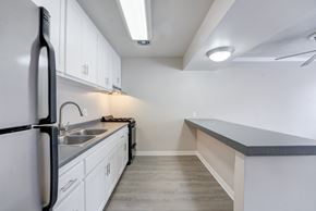 Carlsbad apartment for rent - Apartments in Carlsbad, CA - The Village Apartments - Kitchen Equipped With Double Sink, White Cabinets, Gray Countertops, Stainless Steel Refrigerator, And Breakfast Bar.