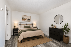 Orlando apartment for rent - A bedroom with a large bed, a nightstand, a lamp, a plant, and a round mirror on the wall.