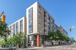Raleigh apartment for rent - A modern multi-story building with a red entrance sits on a street corner.