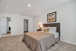 Taylors apartment for rent - Bedroom with tan carpet, white walls, queen bed with brown headboard, butterfly pillow, landscape painting, and open closet door.