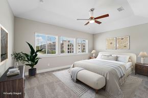 Houston townhouse for rent - A bedroom with a large bed, a ceiling fan, and a view of the city through the windows.
