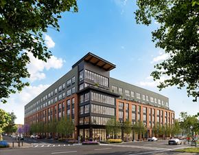 Newark apartment for rent - A modern multi-story building with a mix of glass and brick exterior is surrounded by trees and has a street in front of it.