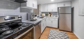 Miami apartment for rent - Modern kitchen with stainless steel appliances, white cabinets, gray backsplash, and wood-look flooring.