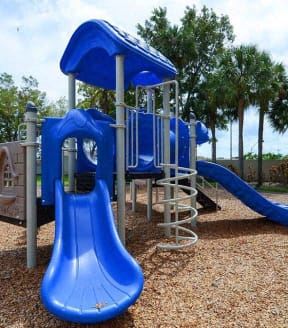 Miami apartment for rent - Blue playground slide and climbing structure on wood chip surface.