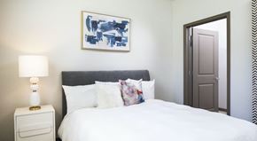 Championsgate apartment for rent - A bedroom with a white bed, a white nightstand with a lamp, and a framed blue and white painting above the bed.