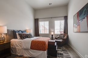 Greeley apartment for rent - One Bedroom Luxury Apartments in Greeley CO - The Shelby - Furnished Bedroom with a Large Bed, a Leather Chair, Two Windows, White Walls, a Wooden Nightstand, and Wood-Style Flooring