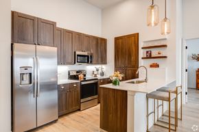 Greeley apartment for rent - Three-Bedroom Luxury Apartments in Greeley, CO - The Shelby - Kitchen With Wood Cabinets, Stainless Steel Appliances, White Countertops, And Breakfast Bar Seating.