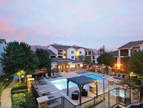 Upland apartment for rent - Pet-Friendly Apartments in Upland, CA - Park Central Apartments - Swimming Pool with a Spa, Sun Loungers, Lounge Seats, Pergola, and Umbrellas, Surrounded by a Metal Fence, Trees, and Landscaping.