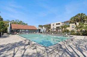 Tampa apartment for rent - A large swimming pool surrounded by a concrete patio and a building in the background.