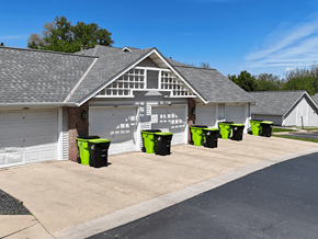 Rochester townhouse for rent - A white building with a black roof and a row of green bins in front.