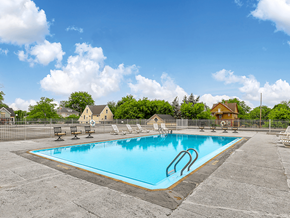 Lansing apartment for rent - A large outdoor swimming pool surrounded by a fence and lounge chairs.