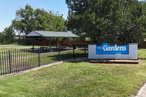 Pueblo apartment for rent - A sign for Mega Gardens stands in front of a fence and trees.