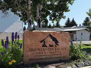 Gunnison apartment for rent - A sign for Mountaineer Village Apartments is surrounded by flowers and trees.
