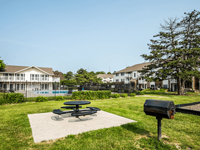 Omaha apartment for rent - a picnic table and grill sit on a concrete slab in a grassy area with a pool