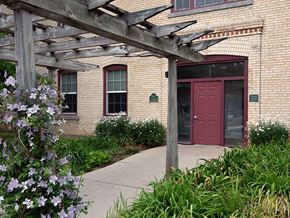 Grand Ledge townhouse for rent - a historic brick building with a red door and a wooden pergola