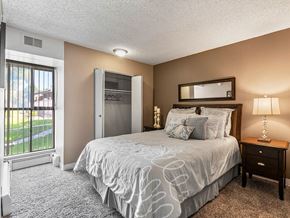 Albuquerque apartment for rent - A bedroom with a large bed, a nightstand, and a window with a view of a lawn.