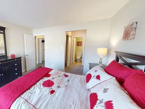 Florissant apartment for rent - A bed with a red and white comforter is in the foreground of a bedroom.