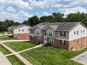 Fenton apartment for rent - A large building with a grey roof and a white door is surrounded by a grassy area.