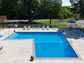 Fenton apartment for rent - A large blue swimming pool surrounded by trees and chairs.