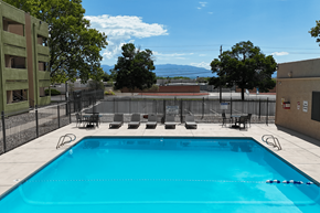 Albuquerque apartment for rent - A blue swimming pool surrounded by a black fence and chairs.