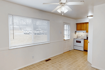 St. Louis apartment for rent - A room with a fan, window with blinds, and a kitchen area with a stove and oven.