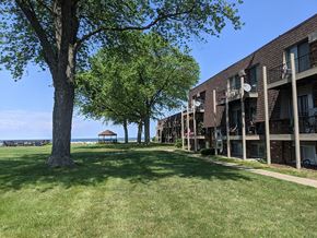 Sandusky apartment for rent - A grassy area in front of a building with a tree and a bench.