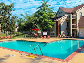 Florissant apartment for rent - A swimming pool with a red umbrella and chairs in front of a building.