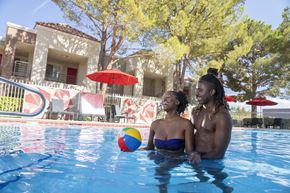 Las Vegas apartment for rent - A couple is sitting in a pool with a ball in the foreground. at Solstice Apartment Homes, Las Vegas, 89108