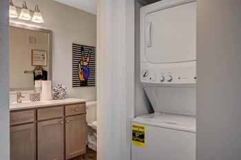 A washing machine is in a small bathroom with a mirror, toilet, and sink.