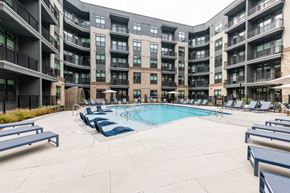 Cary apartment for rent - A large outdoor pool surrounded by lounge chairs and umbrellas in front of apartment buildings.