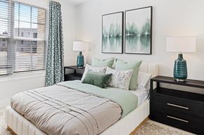 Raleigh apartment for rent - A bedroom with a large bed, two nightstands with lamps, and two framed pictures on the wall at Parker Apartments in Raleigh, NC.