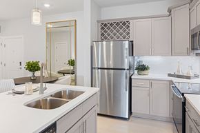 Raleigh apartment for rent - A modern kitchen with a stainless steel refrigerator and a large mirror above the sink at Parker Apartments in Raleigh, NC..