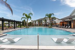 Ocala apartment for rent - A large swimming pool with lounge chairs and a building in the background.
