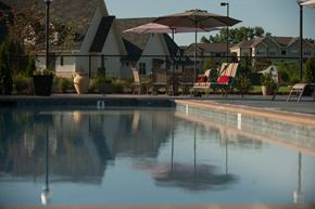 Huntsville apartment for rent - A pool with a reflection of a building and a patio with chairs and umbrellas.