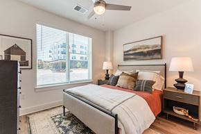 Greensboro apartment for rent - a modern bedroom with a queen bed a picture on the wall and a ceiling fan.