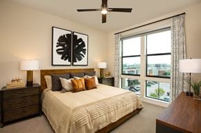 Houston apartment for rent - A bedroom with a large bed, a ceiling fan, and a view of the city at 27Seventy Lower Heights apartments in Houston, TX.