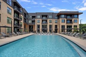Greensboro apartment for rent - A large swimming pool is surrounded by sun loungers in front of a modern building.