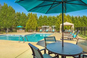 Murfreesboro apartment for rent - A poolside table with chairs and an umbrella overlooking a pool.