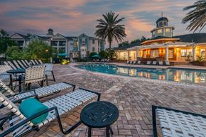 Orange City apartment for rent - A poolside area with lounge chairs and a table in front of a building with a tower.
