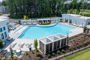 Raleigh apartment for rent - A large outdoor swimming pool surrounded by lounge chairs and trees.