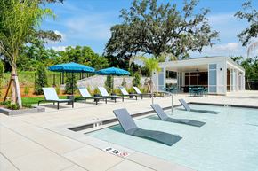 Wildwood apartment for rent - A pool with lounge chairs and umbrellas in front of a white building.
