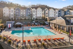 Knoxville apartment for rent - A large swimming pool surrounded by orange chairs in front of apartment buildings at Evergreen at the Bluffs apartments in Knoxville, TN..
