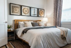 Morehead City apartment for rent - A bedroom with a bed, pillows, a blanket, a nightstand, and a window with curtains.