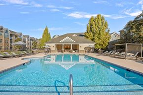 Greensboro apartment for rent - A large swimming pool in front of a building with a poolside lounge.