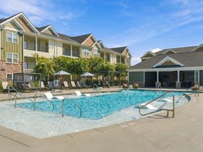 Ooltewah apartment for rent - A swimming pool surrounded by lounge chairs and umbrellas in front of apartment buildings.