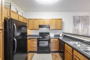 Macon apartment for rent - A black refrigerator stands in a kitchen with wooden cabinets and a black stove.