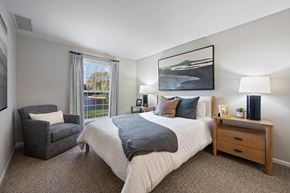 Schaumburg apartment for rent - A bedroom with a large bed, a chair, and a painting on the wall.